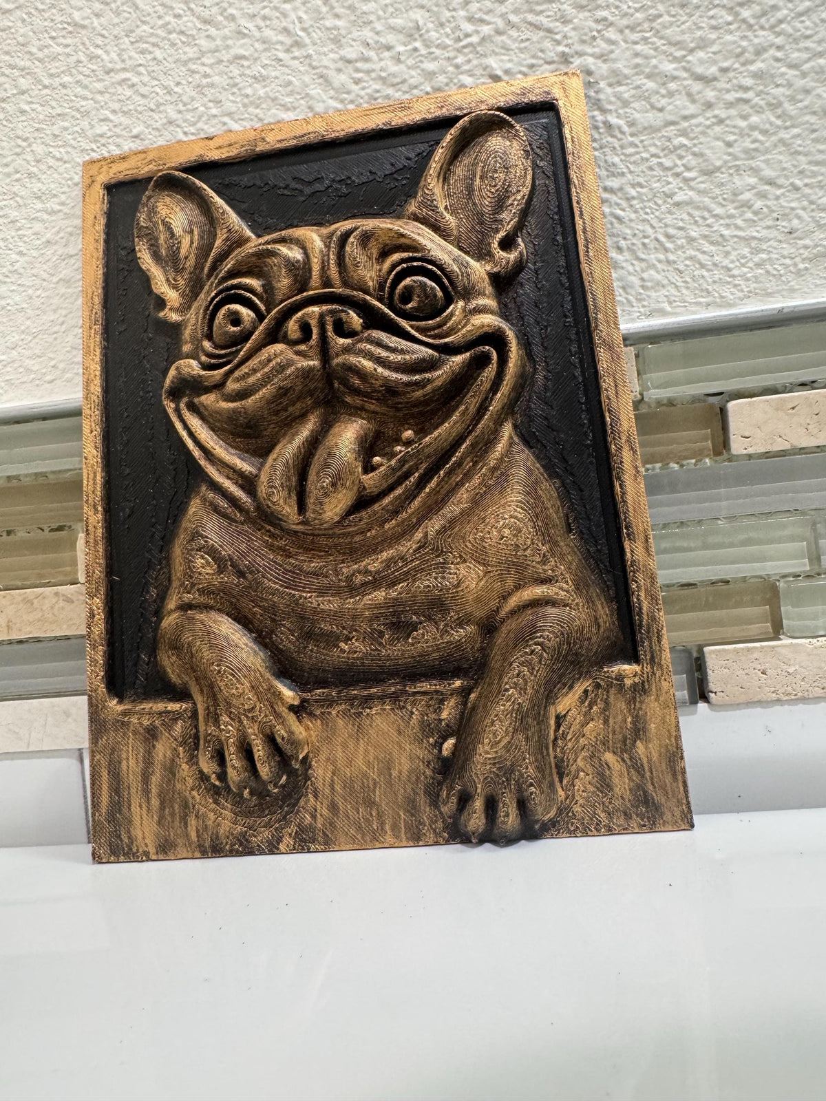 Slight angle of the gold and black bulldog plaque with paws on the ledge
