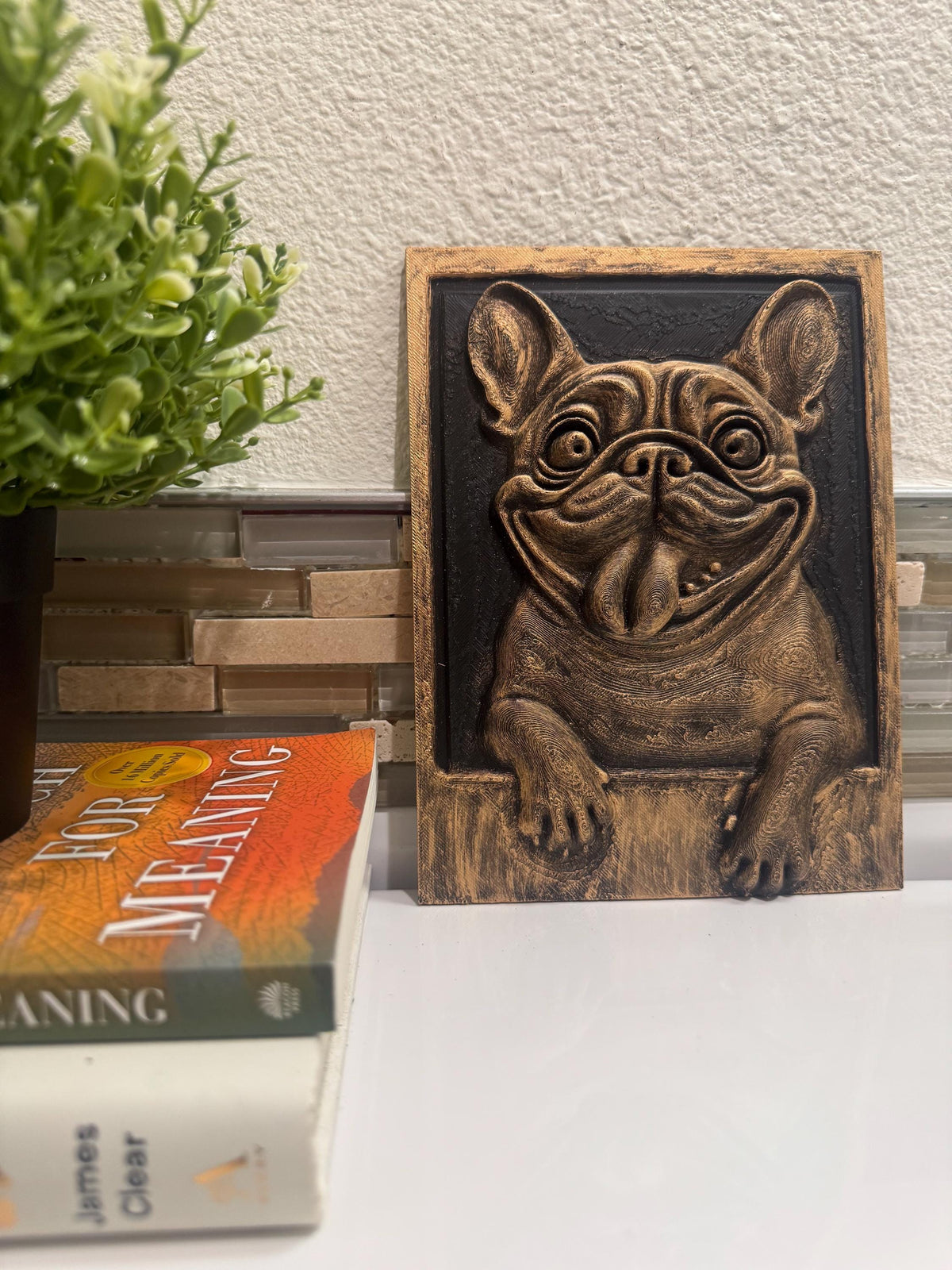 French Bulldog plaque propped beside a plant and books on a counter