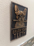 Angled view of the black and gold Frenchie toothbrush plaque on a textured wall