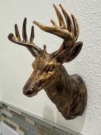Front three-quarter view of antique gold deer head sculpture mounted above tile