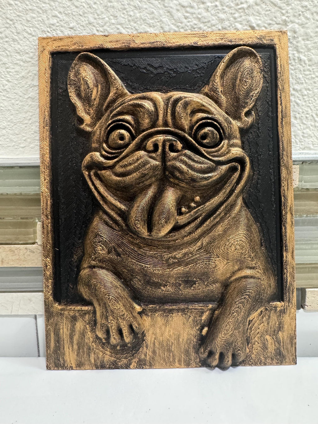 Front view of antique gold French Bulldog plaque with tongue out and paws over the frame