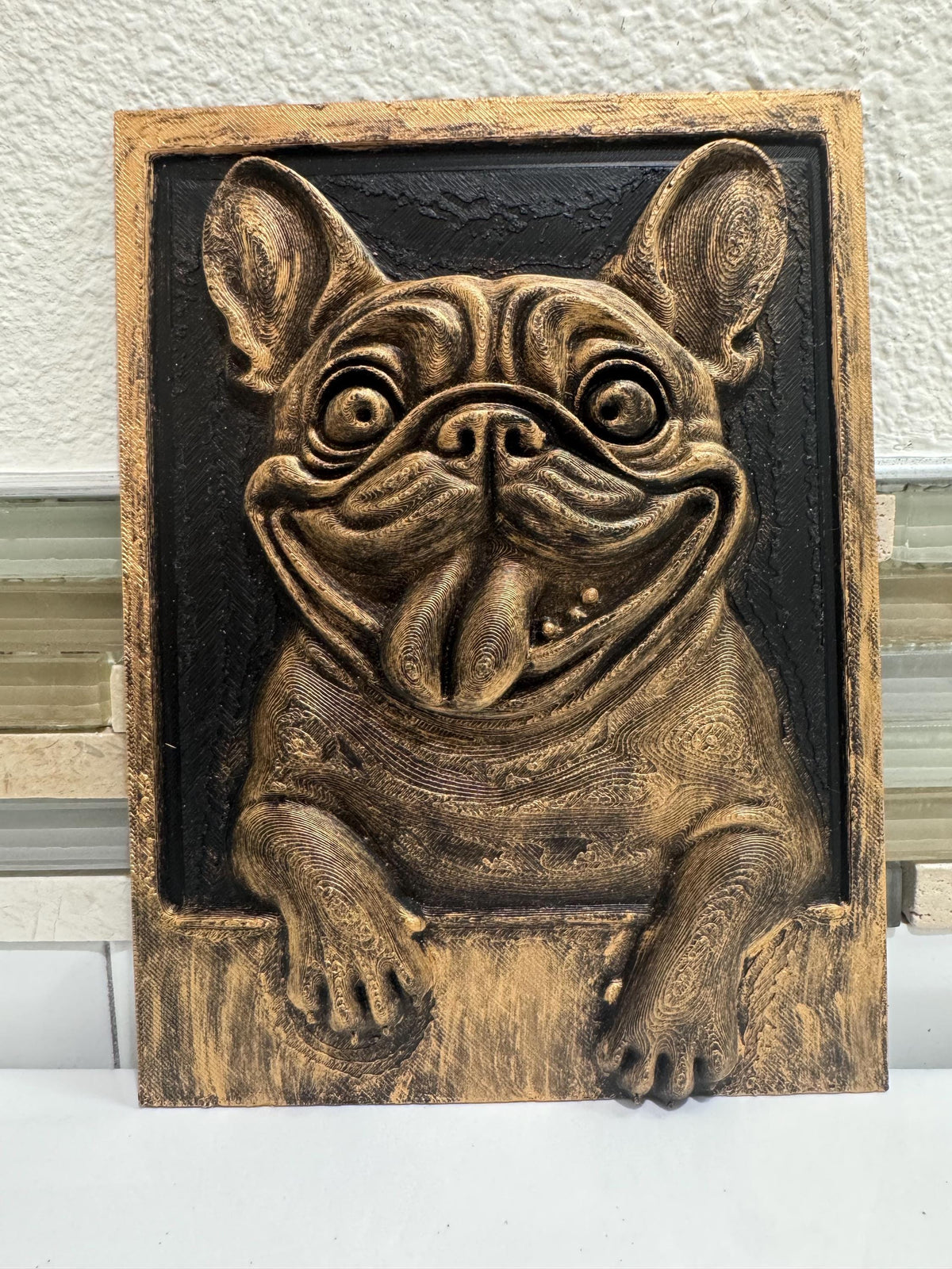 Front view of antique gold French Bulldog plaque with tongue out and paws over the frame