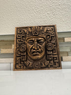 Slight high angle of the bronze Aztec face plaque showing the geometric border