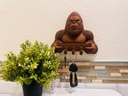Bigfoot key rack on a kitchen wall beside a potted plant with car keys hanging