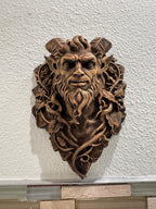 Straight-on view of the bronze demon's intense face surrounded by leaves