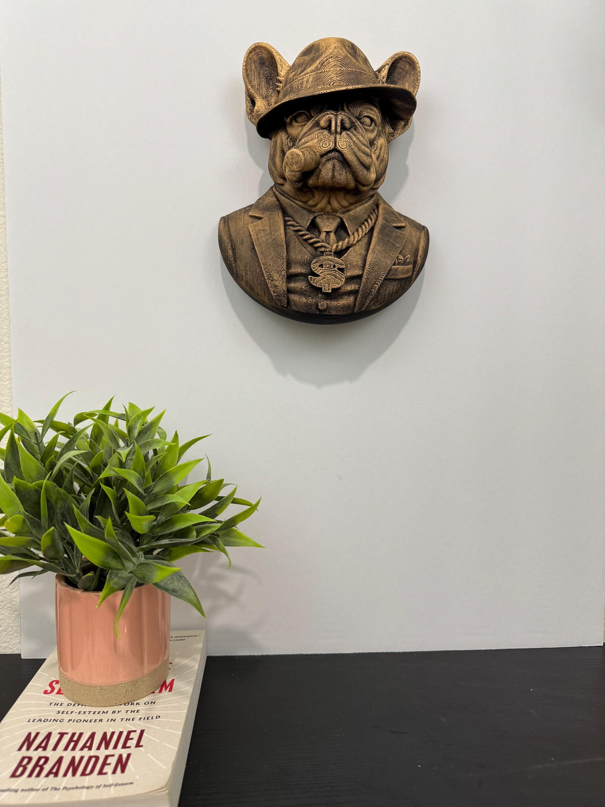 French Bulldog mob boss hung on a wall above a pink potted plant