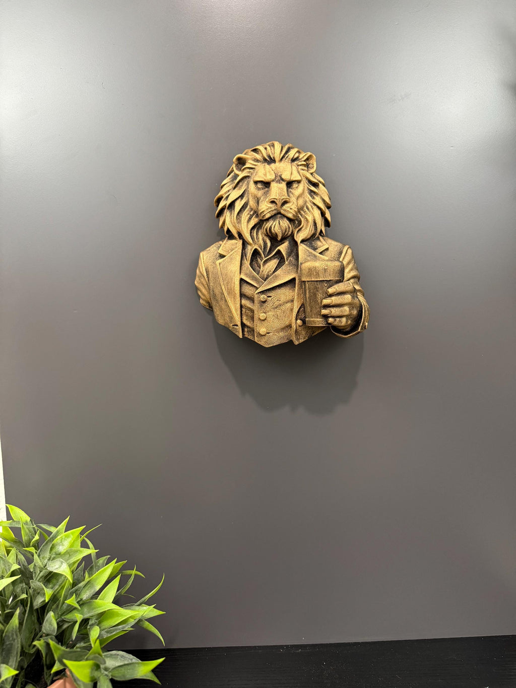 Lion gentleman sculpture hung on a gray wall above a plant