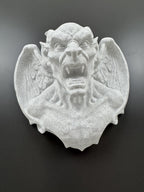 Low front view of the speckled stone gargoyle's snarling face and wing detail