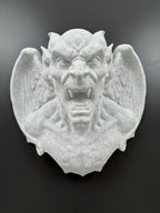 Slight high angle of the gray-white gargoyle bust showing spread wings and fangs