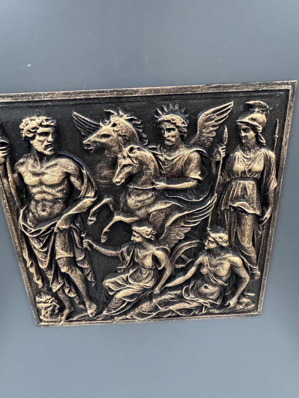 Low angle of the gold mythology relief showing figures and winged horses