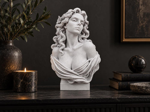 Aphrodite bust on a dark console beside a candle, vase and books