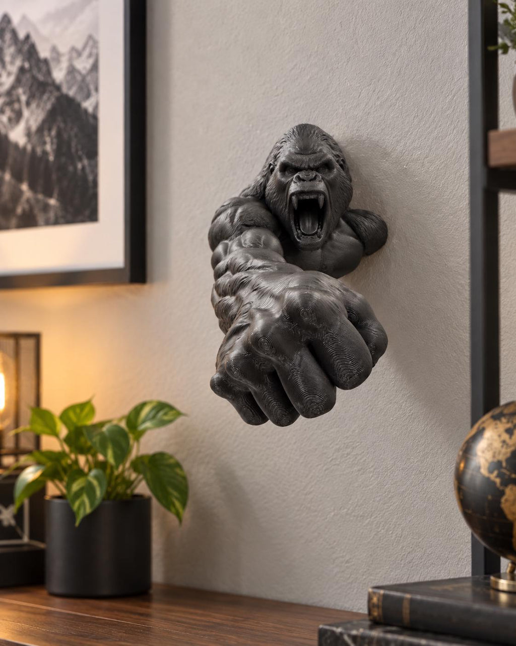 Black gorilla sculpture reaching from a wall above a desk lamp and plant
