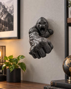 Black gorilla sculpture reaching from a wall above a desk lamp and plant