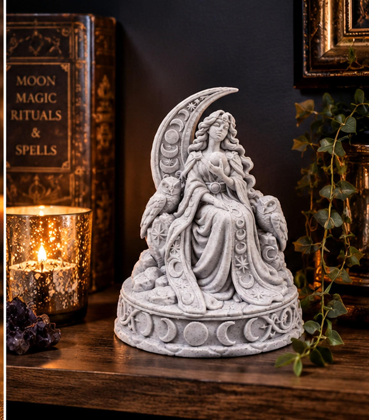 Moon goddess statue on a dark shelf beside a candle and spell books