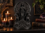 Black Hecate statue on a dark shelf with candles, books and a plant