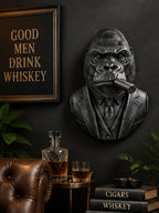 Black gorilla cigar bust on a dark wall above whiskey and a leather chair